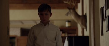 Movie still from “The Strangers” (2008), directed by Bryan Bertino – A young man standing in front of a deer in a room; Medium shot, Over the shoulder angle