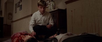 Movie still from “The Strangers” (2008), directed by Bryan Bertino – A young boy sitting on the floor next to a dead body; Medium shot, High angle
