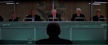Movie still from “The Sum of All Fears” (2002), directed by Phil Alden Robinson – Three men sitting at a table in front of a man in a black suit; Medium shot, Over the shoulder angle