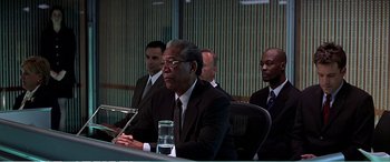 Movie still from “The Sum of All Fears” (2002), directed by Phil Alden Robinson – A group of men sitting at a table in front of a microphone; Medium shot, Over the shoulder angle