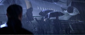 Movie still from “The Sum of All Fears” (2002), directed by Phil Alden Robinson – A group of people standing under an umbrella on an airplane; Wide shot, High angle