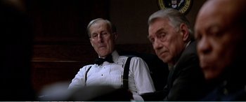 Movie still from “The Sum of All Fears” (2002), directed by Phil Alden Robinson – Two older men sitting in a chair in front of a clock; Medium shot, Low angle