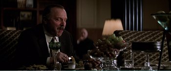 Movie still from “The Sum of All Fears” (2002), directed by Phil Alden Robinson – A man sitting at a table with a glass of wine; Medium shot, Low angle