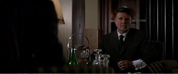 Movie still from “The Sum of All Fears” (2002), directed by Phil Alden Robinson – A man sitting at a table with a glass of wine; Medium shot, Over the shoulder angle