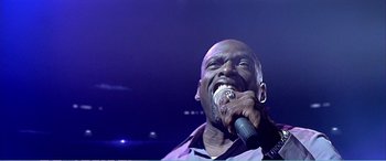 Movie still from “The Sum of All Fears” (2002), directed by Phil Alden Robinson – A man is singing into a microphone on a stage; Close Up shot, Low angle