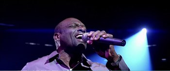 Movie still from “The Sum of All Fears” (2002), directed by Phil Alden Robinson – A man is singing into a microphone on a stage; Close Up shot, Low angle