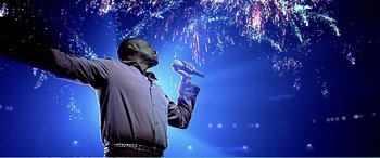 Movie still from “The Sum of All Fears” (2002), directed by Phil Alden Robinson – A man holding a microphone while standing in front of fireworks; Medium shot, Low angle
