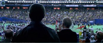 Movie still from “The Sum of All Fears” (2002), directed by Phil Alden Robinson – Two men watching a soccer game in a stadium; Medium shot, Over the shoulder angle