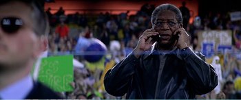 Movie still from “The Sum of All Fears” (2002), directed by Phil Alden Robinson – An older man talking on a cell phone in front of an audience; Close Up shot, Low angle