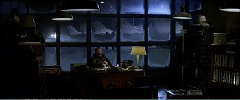 Movie still from “The Sum of All Fears” (2002), directed by Phil Alden Robinson – A man sitting at a desk in front of a large window; Wide shot, High angle