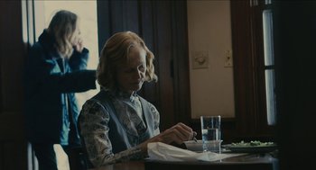 Movie still from “The Taking of Deborah Logan” (2014), directed by Adam Robitel – An older woman sitting at a table with a glass of water; Medium shot, Over the shoulder angle