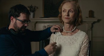 Movie still from “The Taking of Deborah Logan” (2014), directed by Adam Robitel – A man fixing a woman's necklace in a living room; Close Up shot, Over the shoulder angle
