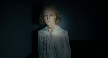 Movie still from “The Taking of Deborah Logan” (2014), directed by Adam Robitel – An older woman is standing in a dark room; Medium shot, Low angle