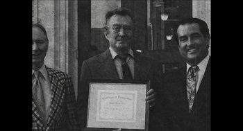 Movie still from “The Taking of Deborah Logan” (2014), directed by Adam Robitel – A man holding up a certificate in front of two other men; Medium shot, Overhead angle