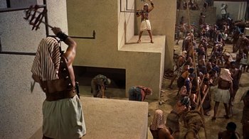 Movie still from “The Ten Commandments” (1956), directed by Cecil B. DeMille – A group of people sitting and standing around a building; Wide shot, High angle