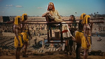 Movie still from “The Ten Commandments” (1956), directed by Cecil B. DeMille – A woman sitting on top of a wooden railing next to a crowd; Wide shot, Low angle