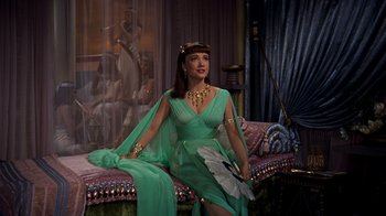 Movie still from “The Ten Commandments” (1956), directed by Cecil B. DeMille – A woman in a green dress sitting on a couch; Medium shot, High angle