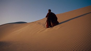 Movie still from “The Ten Commandments” (1956), directed by Cecil B. DeMille – A man in a red robe is sitting in the sand; Extreme Wide shot, Low angle