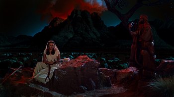 Movie still from “The Ten Commandments” (1956), directed by Cecil B. DeMille – A woman sitting on top of a rock next to a tree; Extreme Wide shot, High angle
