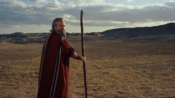 Movie still from “The Ten Commandments” (1956), directed by Cecil B. DeMille – An old man with a long beard holding a stick in the middle of the desert; Wide shot, Low angle