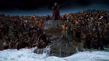 Movie still from “The Ten Commandments” (1956), directed by Cecil B. DeMille – A group of people standing on top of a rock in the water; Extreme Wide shot, High angle