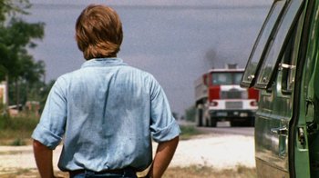 Movie still from “The Texas Chain Saw Massacre” (1974), directed by Tobe Hooper – A man standing in front of a fire truck on the side of the road; Medium shot, Over the shoulder angle