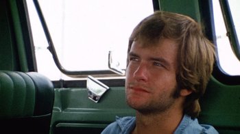 Movie still from “The Texas Chain Saw Massacre” (1974), directed by Tobe Hooper – A man sitting in the back seat of a vehicle; Close Up shot, Low angle