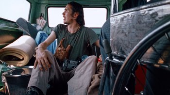 Movie still from “The Texas Chain Saw Massacre” (1974), directed by Tobe Hooper – A man sitting on the back of a vehicle with a cat; Medium shot, Low angle
