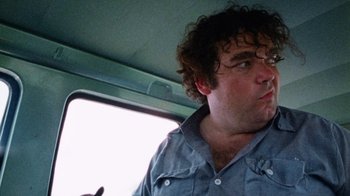Movie still from “The Texas Chain Saw Massacre” (1974), directed by Tobe Hooper – A man with curly hair is looking out the window; Close Up shot, Low angle