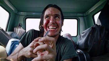 Movie still from “The Texas Chain Saw Massacre” (1974), directed by Tobe Hooper – A man smiles while holding a pen in his mouth; Close Up shot, Low angle