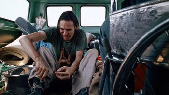 Movie still from “The Texas Chain Saw Massacre” (1974), directed by Tobe Hooper – A man sitting on a bus looking at his cell phone; Medium shot, High angle
