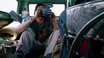 Movie still from “The Texas Chain Saw Massacre” (1974), directed by Tobe Hooper – A man sitting in the back of a vehicle holding a camera; Medium shot, Low angle