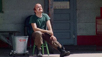 Movie still from “The Texas Chain Saw Massacre” (1974), directed by Tobe Hooper – A man sitting on top of a green chair; Medium shot, High angle