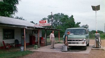 Movie still from “The Texas Chain Saw Massacre” (1974), directed by Tobe Hooper – Two men stand in front of an outdoor barbecue restaurant; Wide shot, Over the shoulder angle