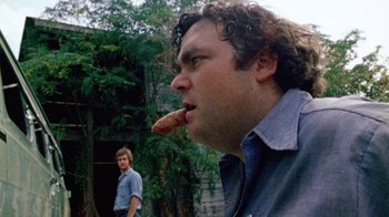 Movie still from “The Texas Chain Saw Massacre” (1974), directed by Tobe Hooper – A man eating a hot dog in front of another man; Close Up shot, Over the shoulder angle