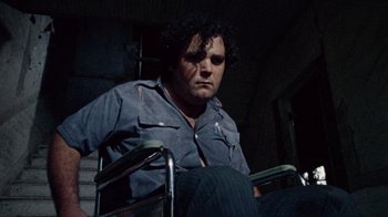 Movie still from “The Texas Chain Saw Massacre” (1974), directed by Tobe Hooper – A man sitting in a chair in a dark room; Medium shot, Low angle