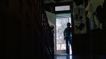 Movie still from “The Texas Chain Saw Massacre” (1974), directed by Tobe Hooper – A man standing in front of an open front door; Wide shot, Low angle