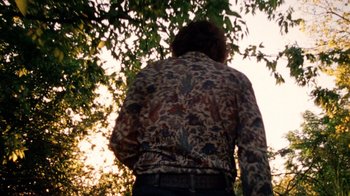Movie still from “The Texas Chain Saw Massacre” (1974), directed by Tobe Hooper – A person standing under a tree wearing a shirt; Medium shot, Low angle