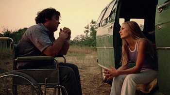 Movie still from “The Texas Chain Saw Massacre” (1974), directed by Tobe Hooper – A man and a woman sitting in front of a green bus; Medium shot, Low angle