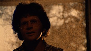 Movie still from “The Texas Chain Saw Massacre” (1974), directed by Tobe Hooper – A man with glasses is standing in front of a wall; Close Up shot, Low angle