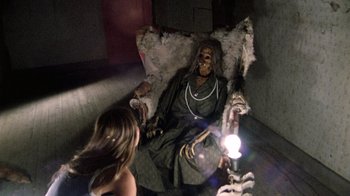 Movie still from “The Texas Chain Saw Massacre” (1974), directed by Tobe Hooper – A woman sitting in a chair next to a skeleton doll; Medium shot, High angle