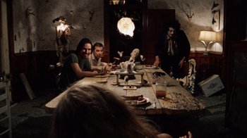 Movie still from “The Texas Chain Saw Massacre” (1974), directed by Tobe Hooper – A group of people sitting at a table with food; Wide shot, Over the shoulder angle
