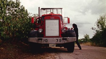 Movie still from “The Texas Chain Saw Massacre” (1974), directed by Tobe Hooper – A man standing in front of a large red truck; Wide shot, Low angle
