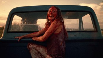 Movie still from “The Texas Chain Saw Massacre” (1974), directed by Tobe Hooper – A woman sitting on the side of a truck with blood on her face; Medium shot, Low angle