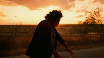 Movie still from “The Texas Chain Saw Massacre” (1974), directed by Tobe Hooper – A person riding a skate board on the side of a road; Medium shot, Low angle