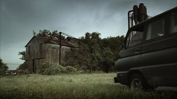 Movie still from “The Texas Chainsaw Massacre” (2003), directed by Marcus Nispel – An old truck parked in the grass near a building; Extreme Wide shot, Low angle
