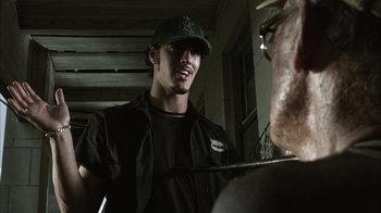 Movie still from “The Texas Chainsaw Massacre” (2003), directed by Marcus Nispel – A man wearing a green hat talking to another man; Medium shot, Over the shoulder angle