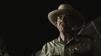 Movie still from “The Texas Chainsaw Massacre” (2003), directed by Marcus Nispel – A man wearing a hat and a uniform looking to his left; Close Up shot, Low angle
