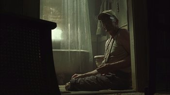 Movie still from “The Texas Chainsaw Massacre” (2003), directed by Marcus Nispel – A man sitting on the ground in a room; Medium shot, Low angle