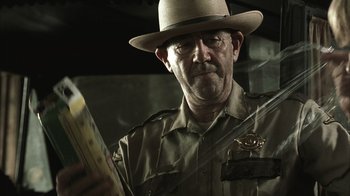 Movie still from “The Texas Chainsaw Massacre” (2003), directed by Marcus Nispel – A man in a hat is looking at a book; Close Up shot, Low angle